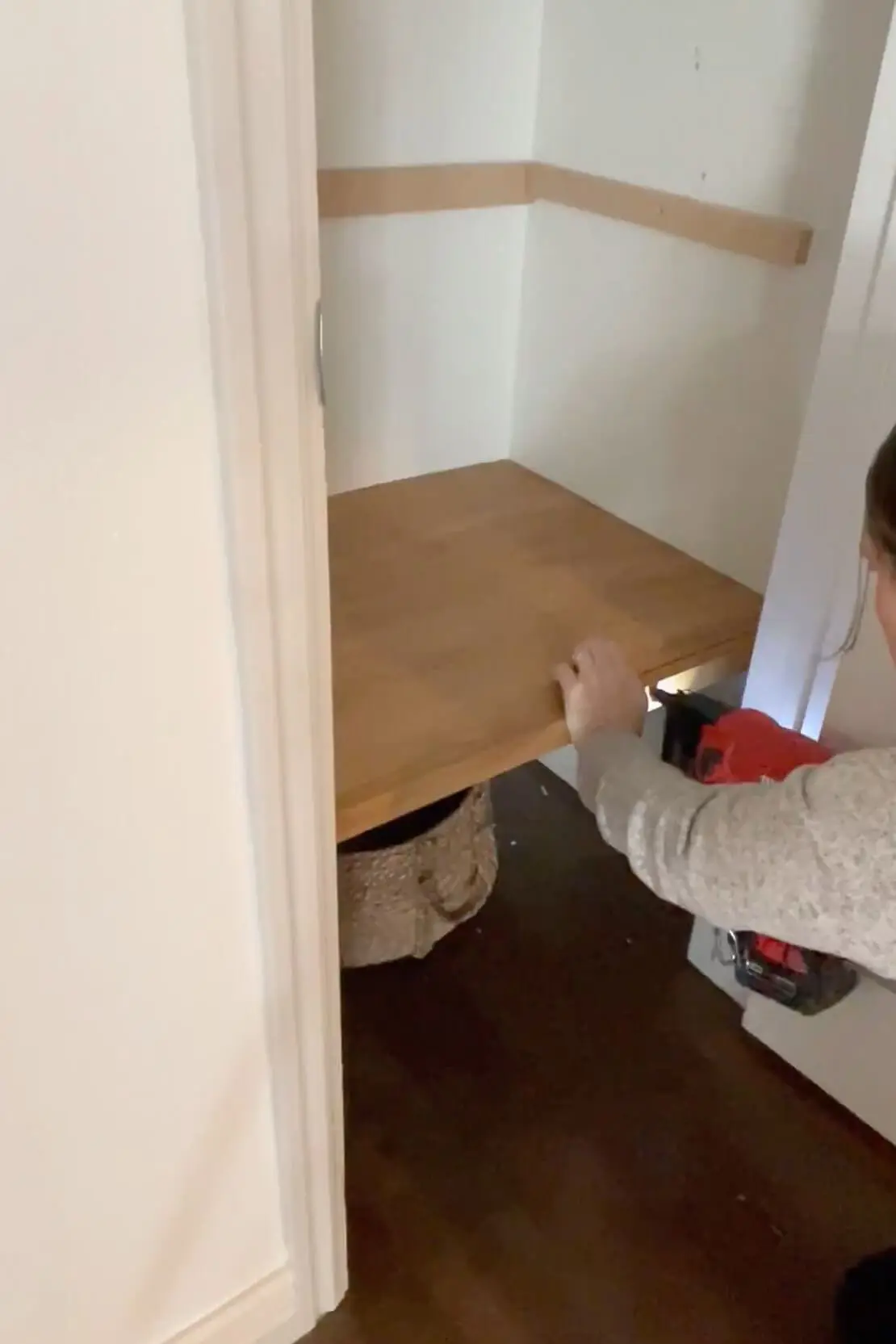 A DIYer secures a custom wooden shelf in a closet, using a nail gun to reinforce the installation.